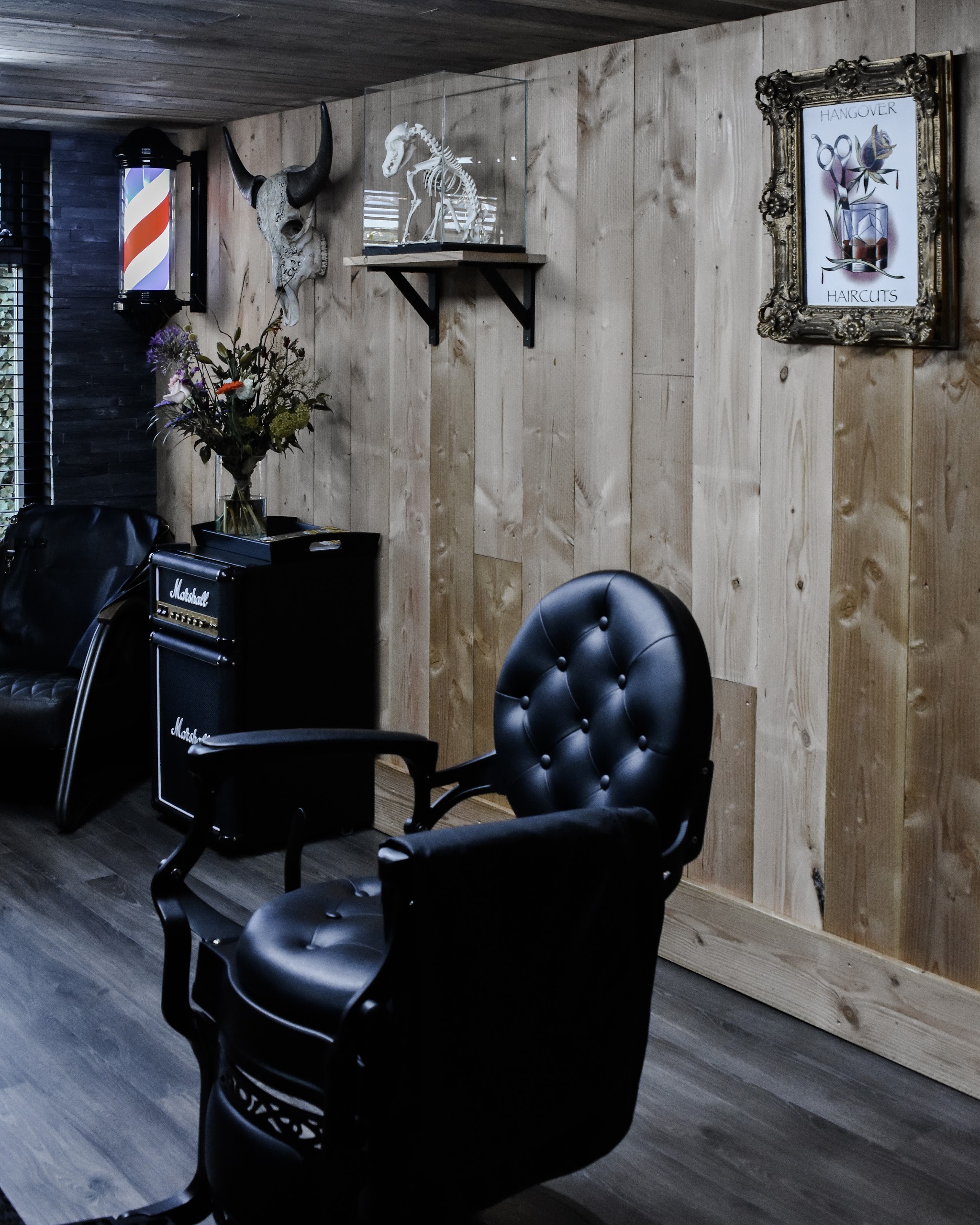 De zwarte barberstoel voor de houten wand, met een Marshall versterker en ingelijste kunst