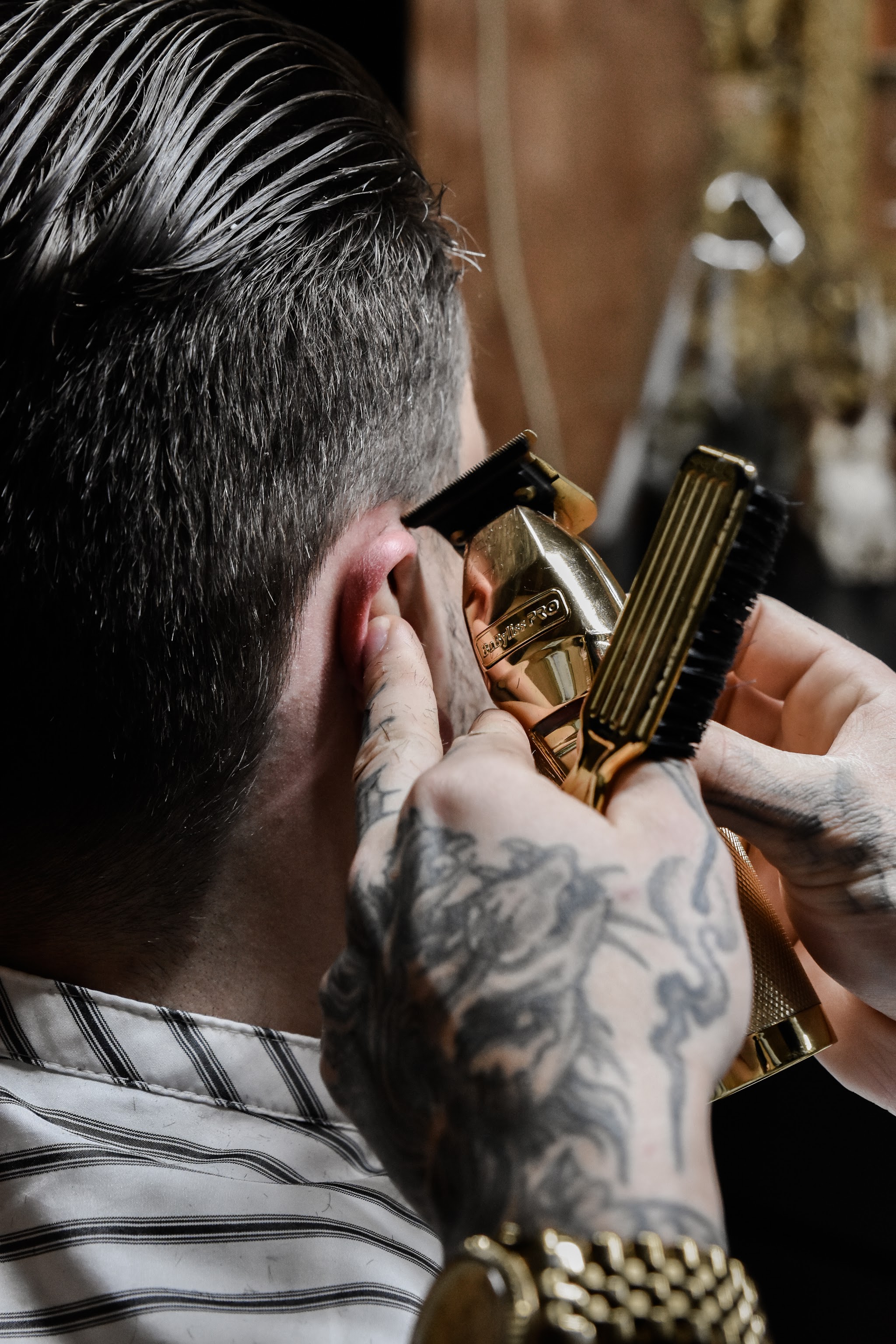 Daan zet met een gouden tondeuse de contour bij het oor van een klant